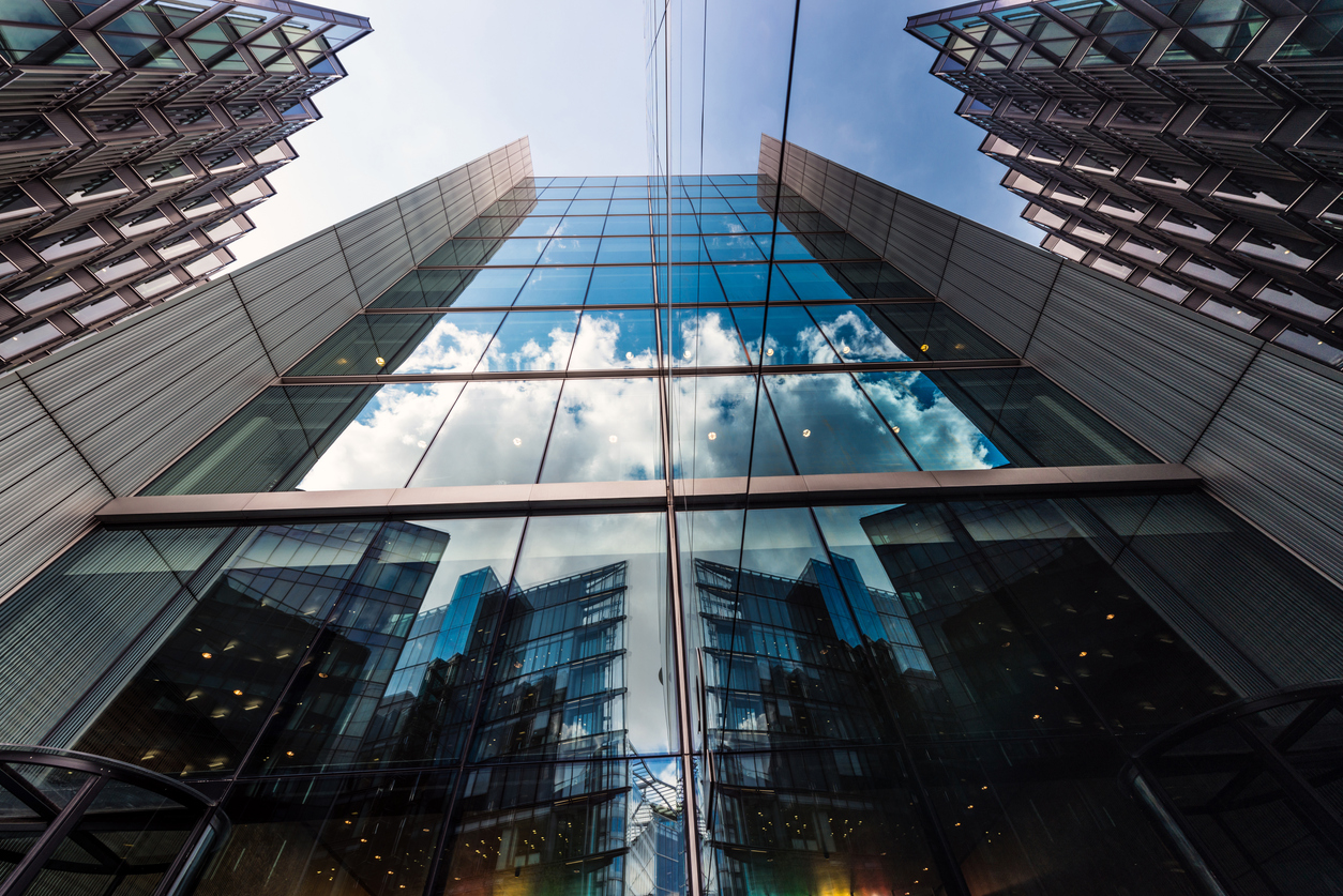 Upward view of glass-and-steel financial district office towers reflecting sky and clouds, representing the institutional strength of the world's largest life insurance companies